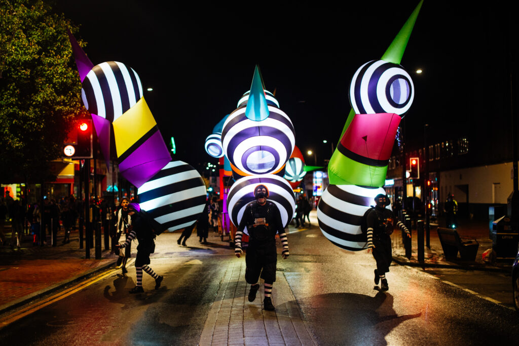 Three colourful inflatable sculptures walking down a dark street