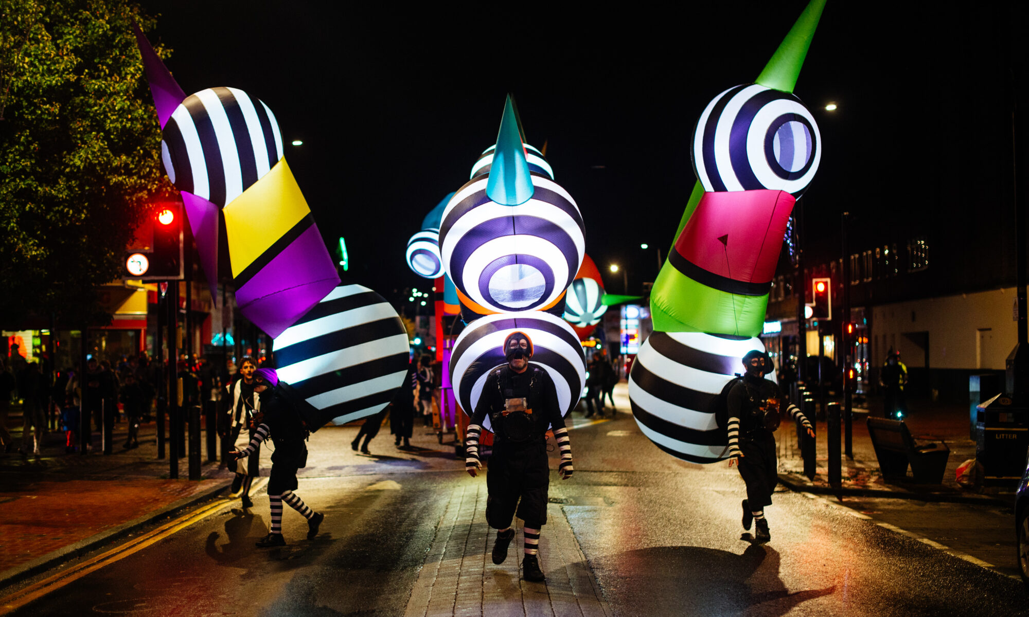 Three colourful inflatable sculptures walking down a dark street