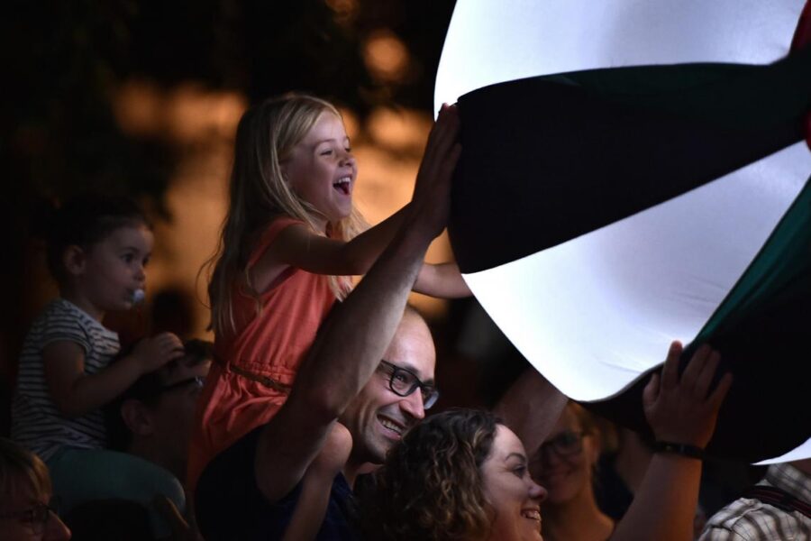 Young girl sits on a man's shoulders to touch an illuminated ball