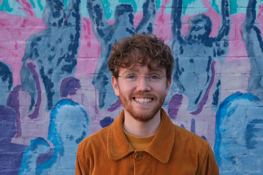 Smiling man standing in front of a colourful mural